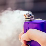 purple vape in a man's hand on a modern background.