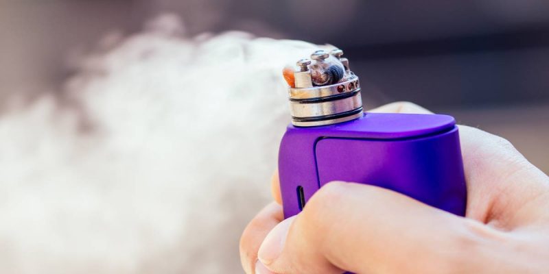 purple vape in a man's hand on a modern background.