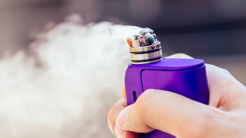 purple vape in a man's hand on a modern background.