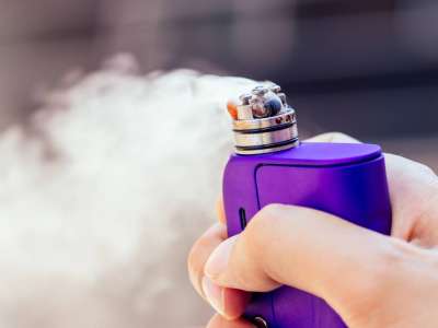 purple vape in a man's hand on a modern background.