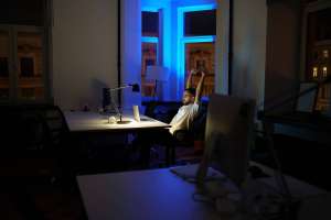 Male freelancer work late night stretching hands and back while sitting at laptop computer in dark office. Tired man programmer web designer overtime within deadline. Exhausted developer having break (Male freelancer work late night stretching hands a