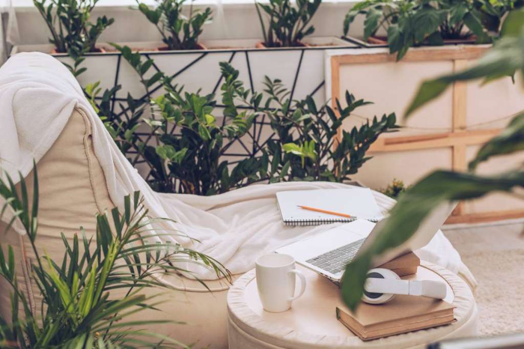 selective focus of laptop, headphones and coffee cup on pouf near soft chaise lounge surrounded by